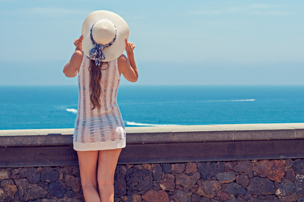 Lady Looking Out At Shore With Sun Hat on Her Head | Oceans Travel